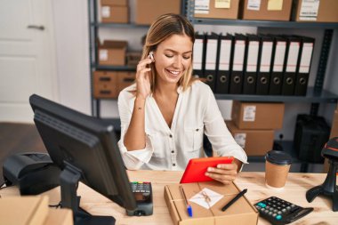 Latin kökenli genç bir kadın iş kadını dokunmatik ped kullanarak ofiste müzik dinliyor.