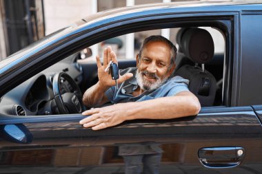 Yaşlı gri saçlı adam gülümsüyor. Elinde yeni arabanın anahtarı var.