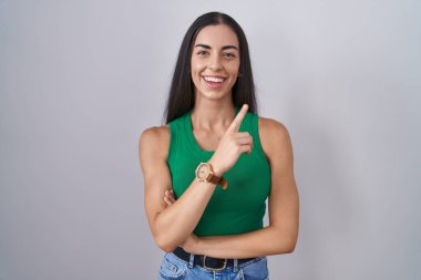 İzole edilmiş arka planda duran genç bir kadın yüzünde kocaman bir gülümsemeyle, kameraya el ile işaret ederek bakıyor.. 