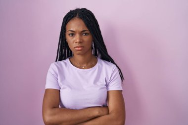 African american woman with braids standing over pink background skeptic and nervous, disapproving expression on face with crossed arms. negative person. 