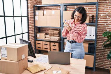 Young woman ecommerce business worker writing on reminder paper at office