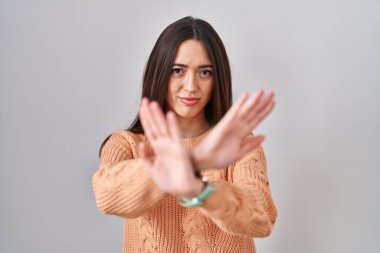Young brunette woman standing over white background rejection expression crossing arms and palms doing negative sign, angry face 
