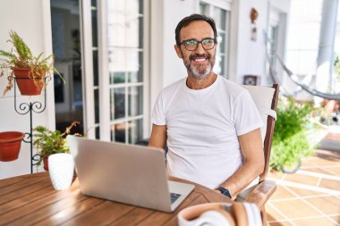 Middle age man using computer laptop at home smiling looking to the side and staring away thinking. 
