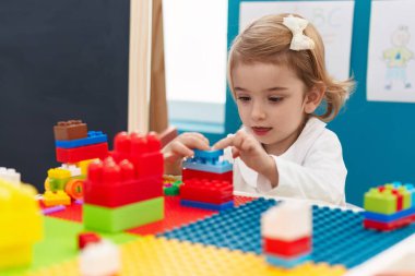Adorable caucasian girl playing with construction blocks sitting on table at kindergarten