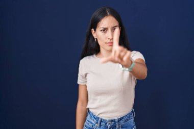 Mavi arka planda duran genç İspanyol kadın parmağını kaldırmış ve kızgın bir ifadeyle işaret ediyor, hiçbir hareket göstermiyor. 