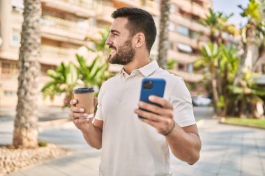 Genç İspanyol adam akıllı telefon kullanıyor, sokakta kahve içiyor.