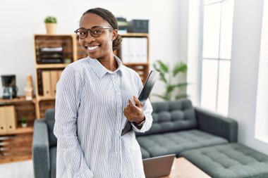 African woman working at psychology clinic looking away to side with smile on face, natural expression. laughing confident. 