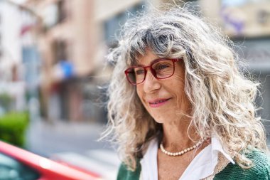Orta yaşlı kadın sokakta kendine güvenen gözlüklü gülümsüyor.