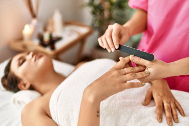 Young beautiful hispanic woman lying on table having manicure treatment at beauty salon