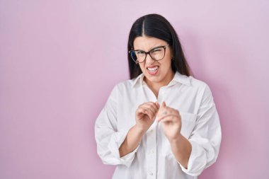 Pembe arka planda duran esmer kadın tiksinti ifadesi, tiksinti tepkisi yüzünden tiksinti ve korku dolu bir ifade. Eller havada. 