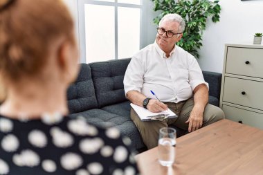 Senior psychologist man at consultation office smiling looking to the side and staring away thinking. 