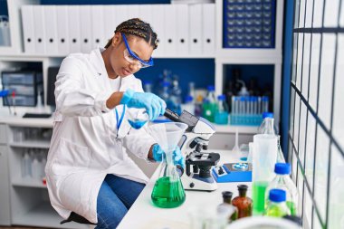 Laboratuvarda test tüpüne sıvı döken Afrikalı Amerikalı kadın bilim adamı.