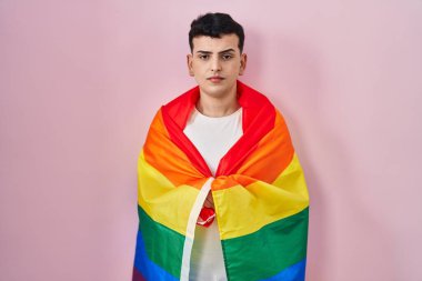 Non binary person holding rainbow lgbtq flag thinking attitude and sober expression looking self confident 