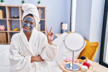 Siyah saçlı, güzel maske takan, gülümseyen, kameraya göz kırpan, zafer işareti yapan İspanyol kadın. İki numara.. 