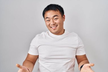 Young chinese man standing over white background smiling cheerful with open arms as friendly welcome, positive and confident greetings 