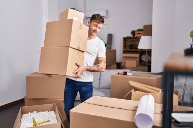 Genç adam yeni evinde paketleri tutarken kendinden emin gülümsüyor.