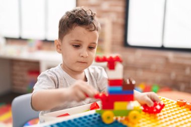 Adorable hispanic toddler playing with construction blocks sitting on table at kindergarten