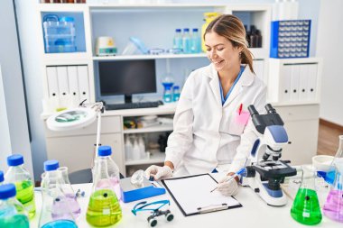 Young hispanic woman scientist weighing diamond writing report at laboratory
