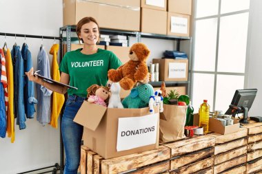 Gönüllü üniforma giyen genç bir kadın hayır kurumunda panoya yazı yazıyor.