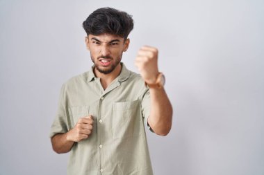 Arab man with beard standing over white background angry and mad raising fist frustrated and furious while shouting with anger. rage and aggressive concept. 