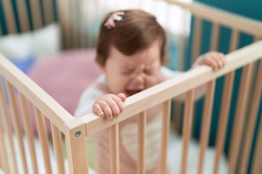 Adorable toddler standing on cradle crying at bedroom