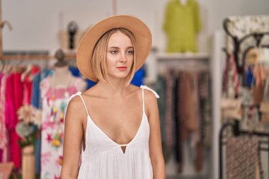 Young blonde woman customer wearing summer hat standing at clothing store