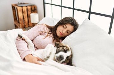 Genç bir kadın yatak odasında bir köpekle yatakta uyuyor.