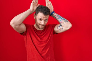 Genç İspanyol adam kırmızı arka planda duruyor. Tavşan kulakları yapıyor. Avuçlarında alaycı ve şüpheci bakışlar var. Paskalya tavşanı konsepti. 