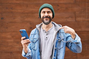Young hispanic man using smartphone pointing finger to one self smiling happy and proud 