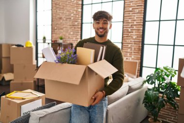 Young arab man smiling confident holding package at new home