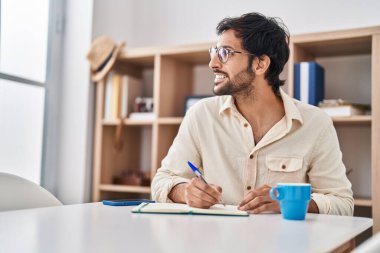 Young hispanic man writing on notebook at home