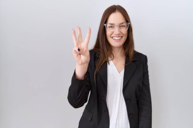 Beautiful brunette woman wearing business jacket and glasses showing and pointing up with fingers number three while smiling confident and happy. 