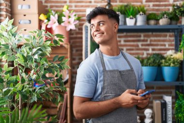 Çiçekçide akıllı telefon kullanarak gülümseyen İspanyol çiçekçi.