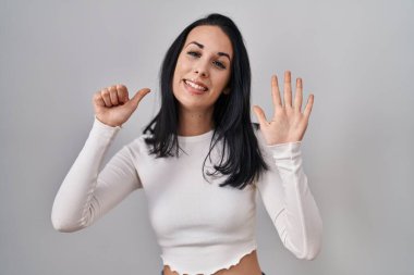 Hispanic woman standing over isolated background showing and pointing up with fingers number six while smiling confident and happy. 