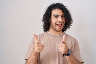 Hispanic man with curly hair standing over white background pointing fingers to camera with happy and funny face. good energy and vibes. 