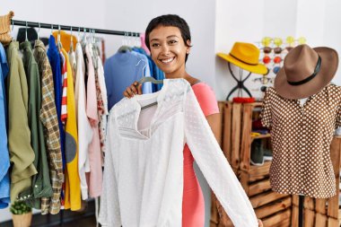 Genç İspanyol kadın müşteri gülümsüyor. Kıyafet seçiyor. Kıyafet dükkanında.