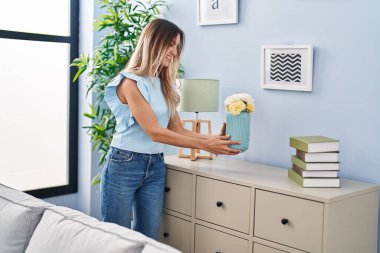 Young woman smiling confident holding plant pot at home