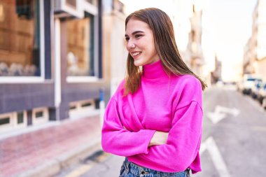 Kendine güvenen genç bir kadın caddede kollarını kavuşturmuş duruyor.