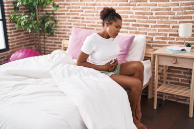 African american woman suffering for menstrual pain sitting on bed at bedroom