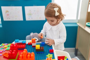 Sevimli beyaz kız anaokulunda duran inşaat bloklarıyla oynuyor.