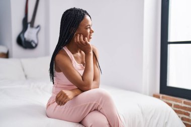 Afro-Amerikalı kadın yatakta kendinden emin bir şekilde gülümsüyor.