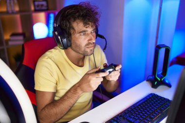 Young hispanic man streamer playing video game using joystick at gaming room