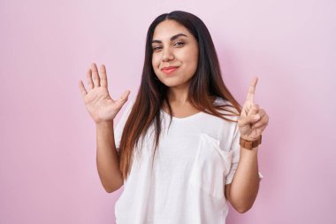 Young arab woman standing over pink background showing and pointing up with fingers number six while smiling confident and happy. 