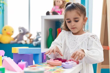 Adorable hispanic girl playing with toys standing at kindergarten