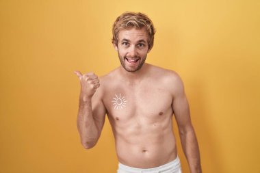 Caucasian man standing shirtless wearing sun screen doing happy thumbs up gesture with hand. approving expression looking at the camera showing success. 