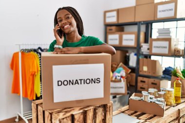 Gönüllü üniforma giyen genç Afro-Amerikan kadın yardım merkezindeki akıllı telefondan konuşuyor.