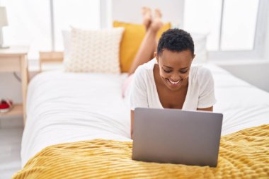 African american woman using laptop lying on bed at bedroom