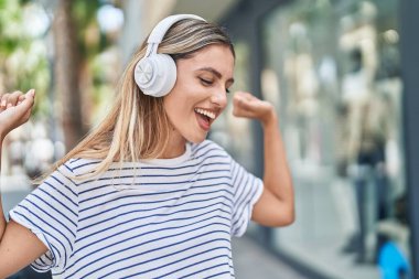 Young blonde woman listening to music and dancing at street
