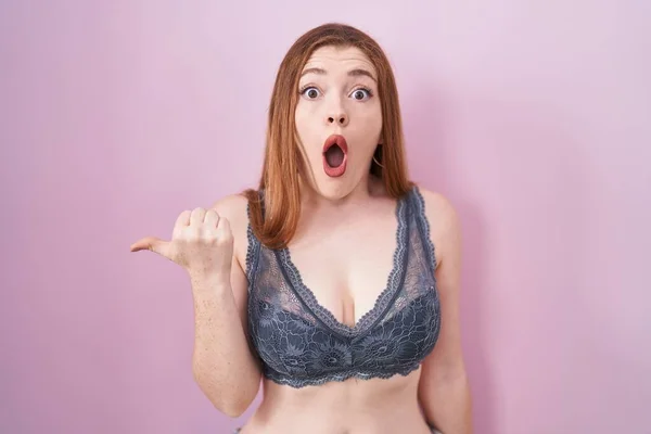 Redhead Woman Wearing Lingerie Pink Background Surprised Pointing Hand Finger — Stockfoto