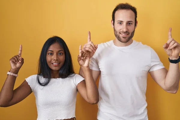 Interracial Couple Standing Yellow Background Smiling Amazed Surprised Pointing Fingers —  Fotos de Stock
